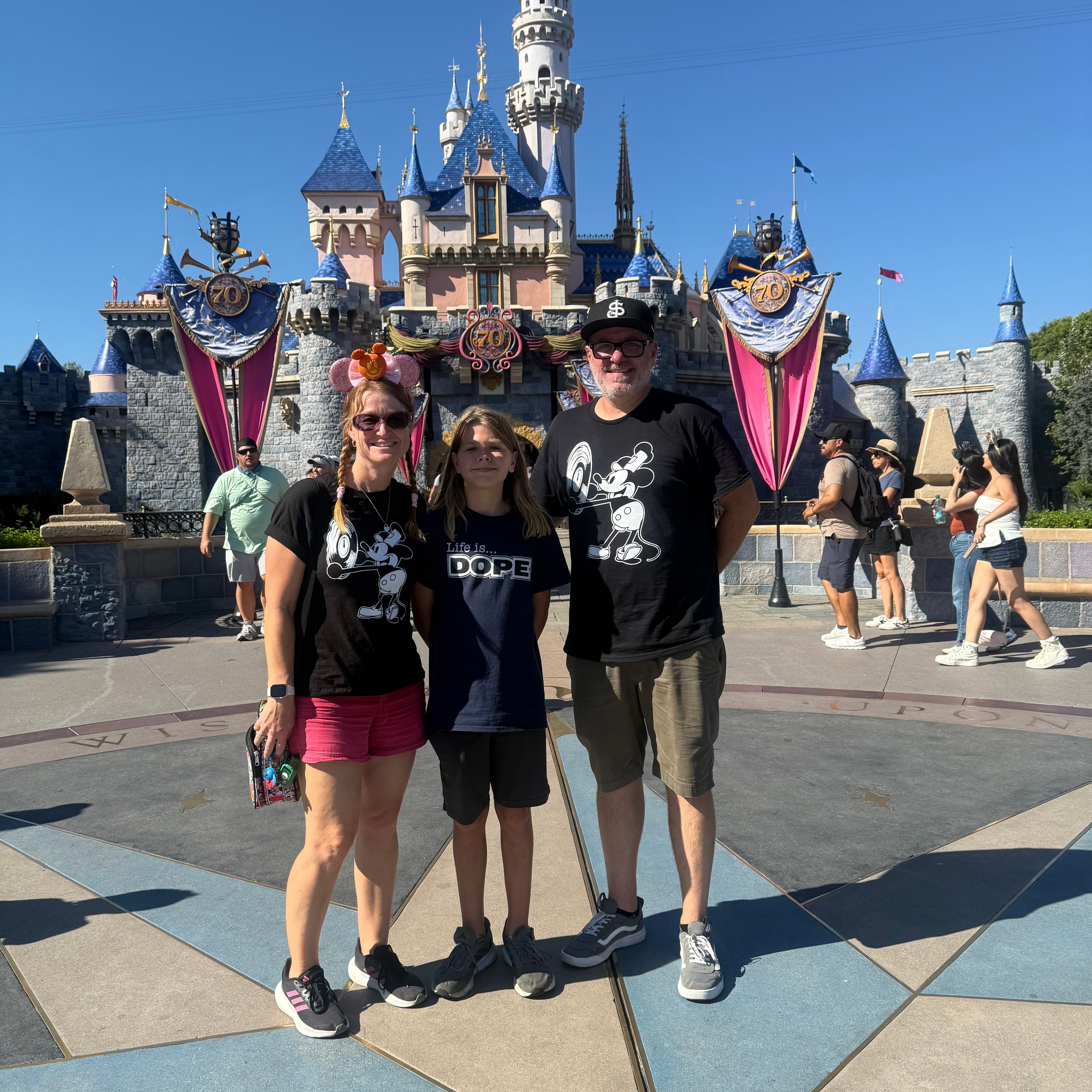 Three people posing in front of a castle at Disneyland in mickey shirts