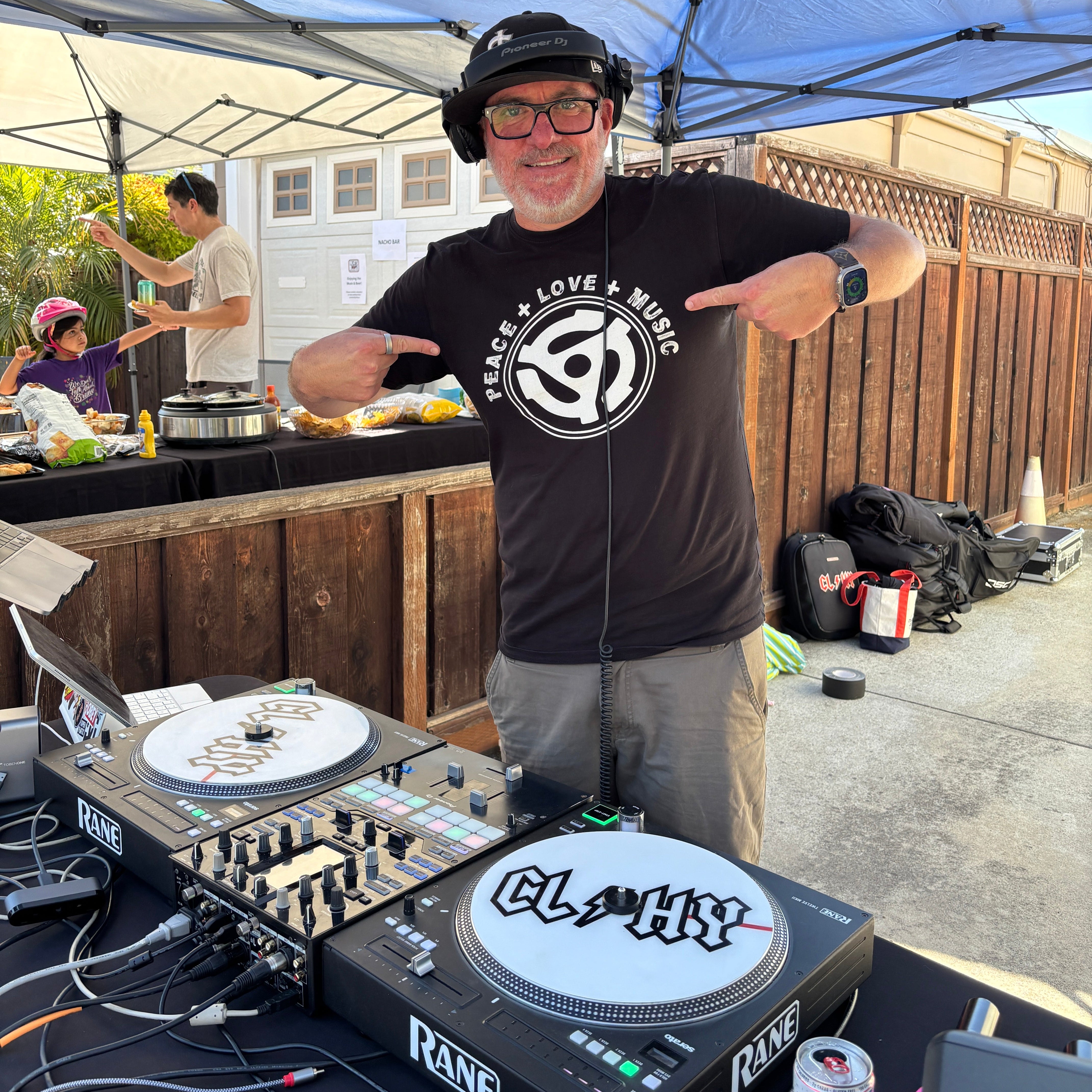DJ at a music event with equipment and people in the background