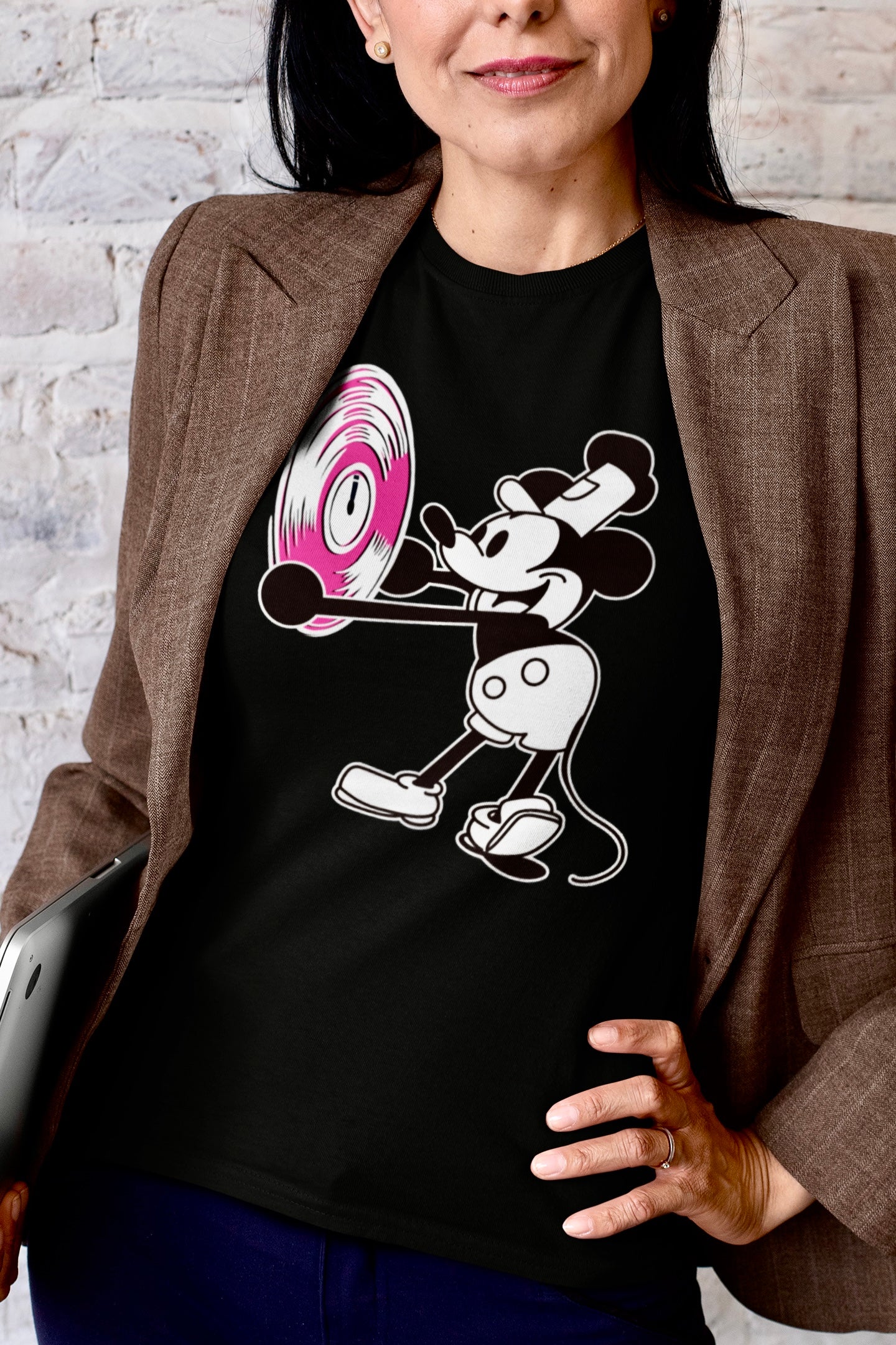 Person wearing a black t-shirt with a cartoon character holding a vinyl record against a brick wall.